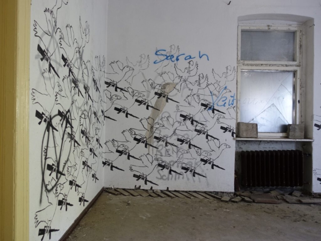 Antje Scholz | Friedensbringer - Malerei über vorhandene Graffiti, im Raum mit der Fluchttreppe, mit Scherben, Holzresten und Schmutz. 2023